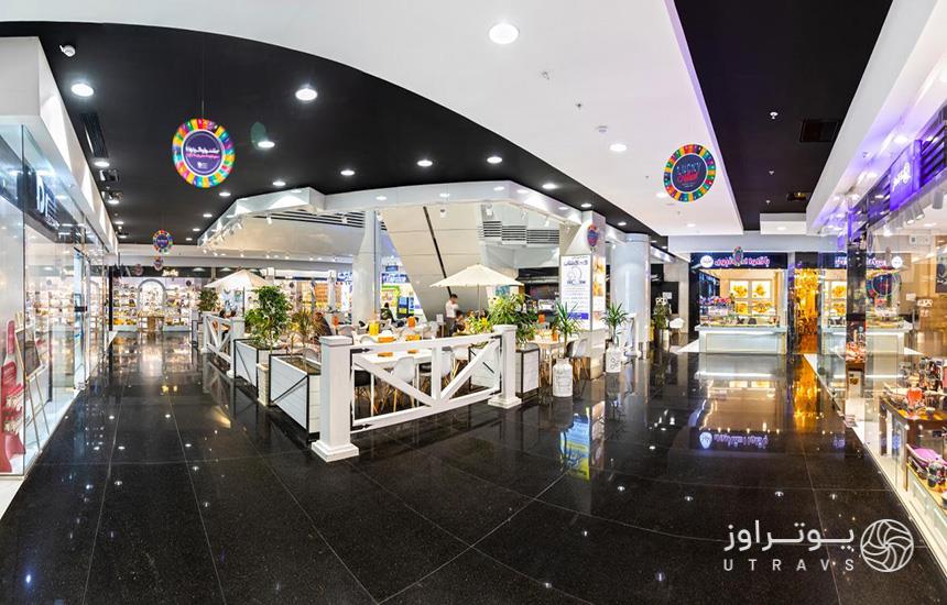 داخل برج آرمیتاژ گلشن مشهد که کف‌پوشی از سرامیک مشکی، کافی‌شاپی در وسط و دورتادور مغازه دارد. 